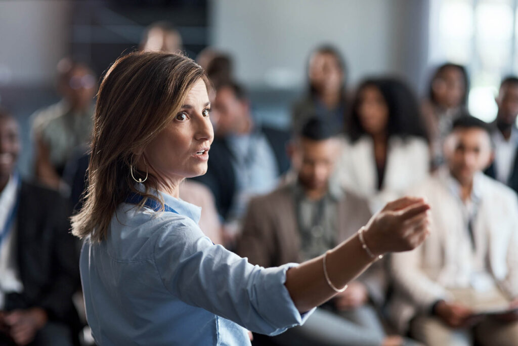 Une femme parle devant un public attentif lors d'une conférence ou d'un séminaire.