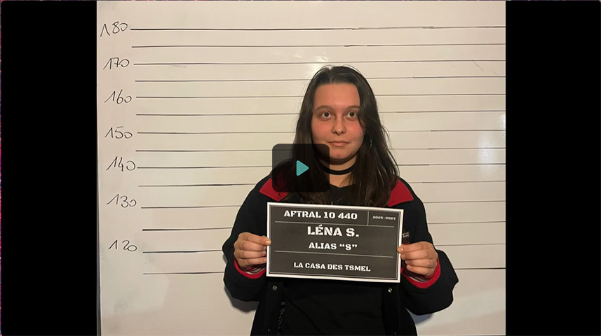 Une jeune fille se tient devant une ligne de mesure avec une plaque indiquant son nom et un alias.