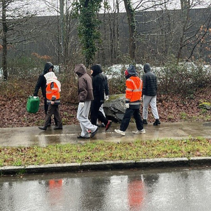 Un groupe de personnes portant des vestes orange marche le long d'un chemin, avec des arbres et un sol humide autour d'eux.