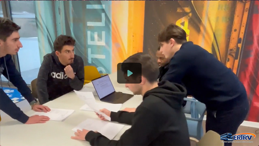 Un groupe de jeunes hommes est réuni autour d'une table avec un ordinateur portable, discutant et examinant des documents dans un environnement coloré.
