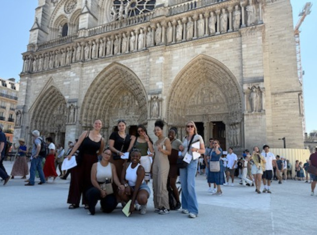 Un groupe de jeunes femmes pose devant la cathédrale Notre-Dame à Paris, entourées de visiteurs et de l'architecture gothique de l'édifice.