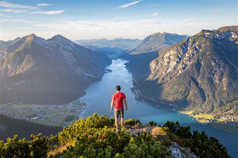 Un homme se tient au sommet d'une montagne, contemplant un paysage spectaculaire de vallées et de lacs entourés de montagnes majestueuses.