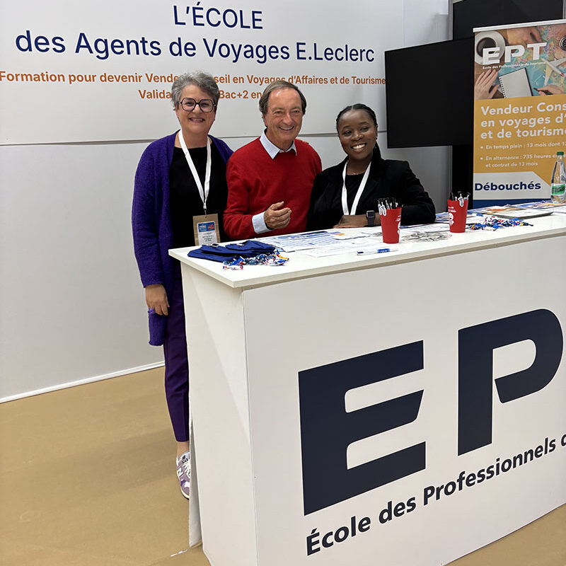 Trois personnes souriantes se tiennent devant un stand de l'École des Agents de Voyages E. Leclerc, présentant des informations sur la formation en tourisme et vente.