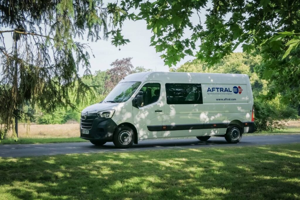 Un camion de la marque Renault, aux couleurs de l'entreprise AFTRAL, est garé sur une route bordée d'arbres et de verdure.