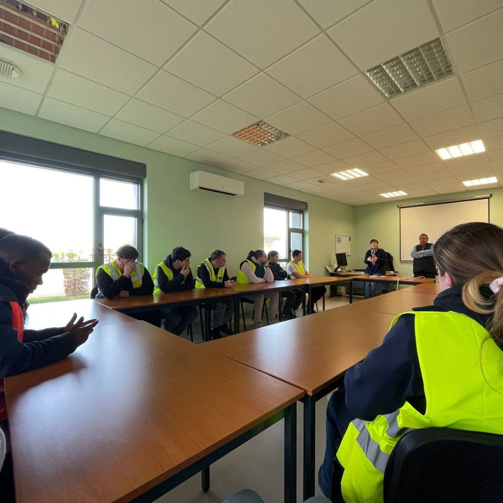 Une réunion se déroule dans une salle avec des participants portant des gilets fluorescents, assis autour d'une grande table.